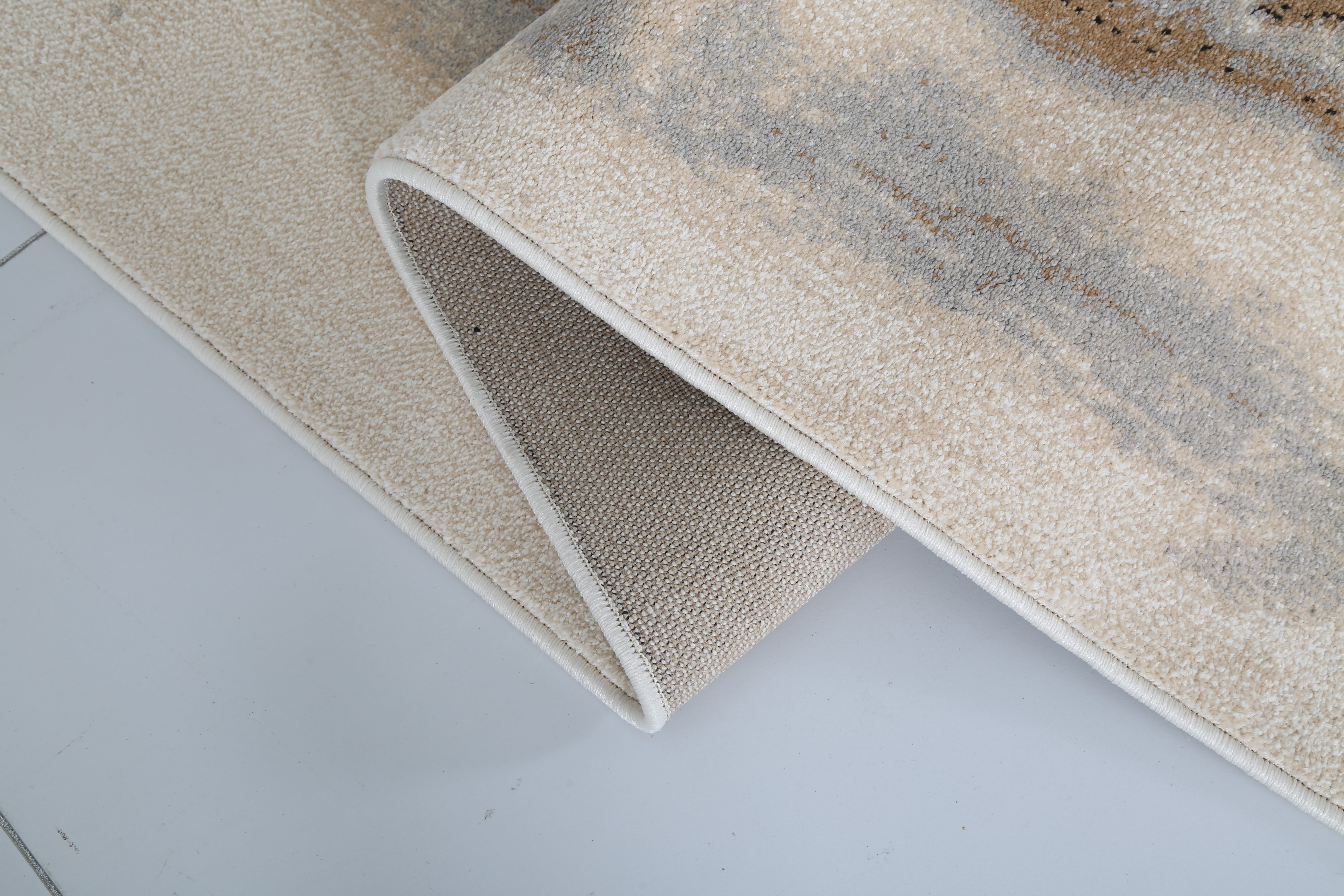 Close-up of a textured beige and brown area rug on a light gray floor.