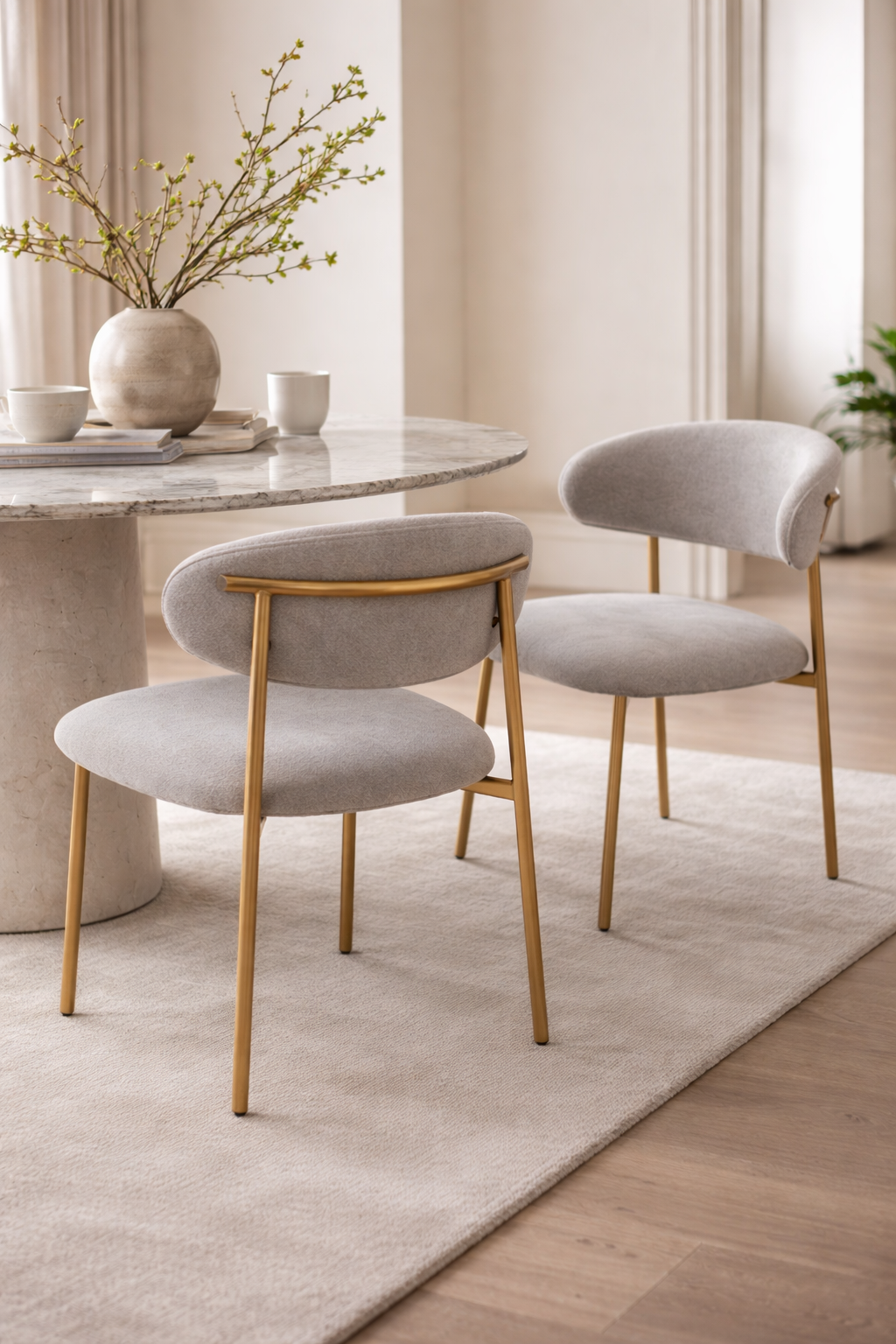 Dining room with round marble table and gray chairs with gold legs.
