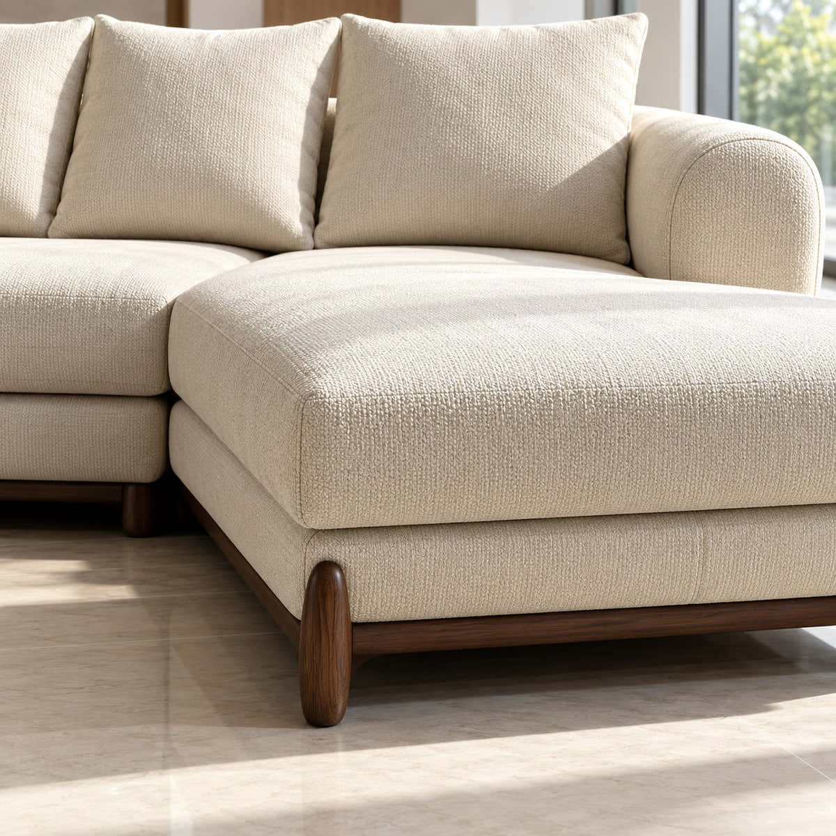 A close-up of a modern sectional sofa in a warm off-white textured fabric, showing the chaise lounge, back cushions, and dark wood legs on a light tiled floor.