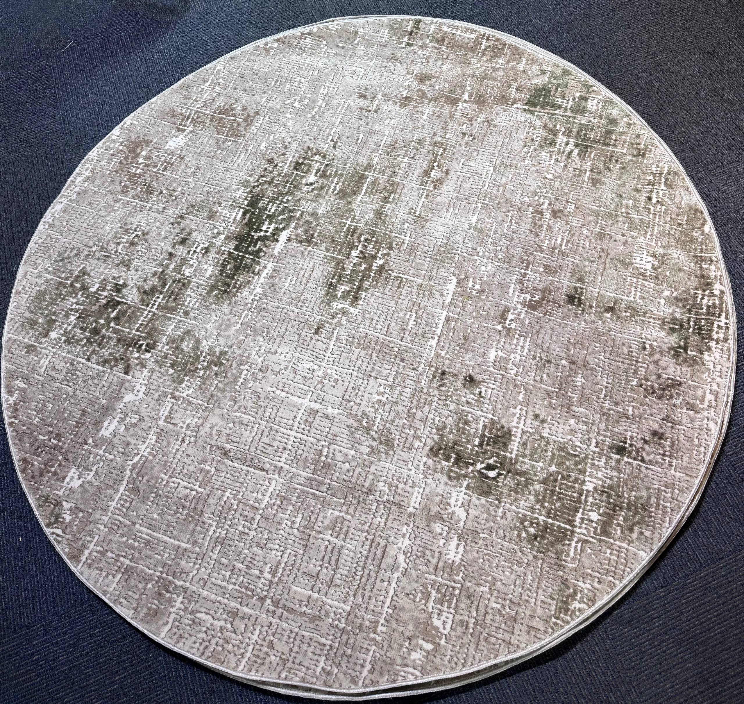 A round area rug with a distressed, vintage-style pattern in shades of gray, beige, and white, laid flat on a dark navy blue fabric background.
