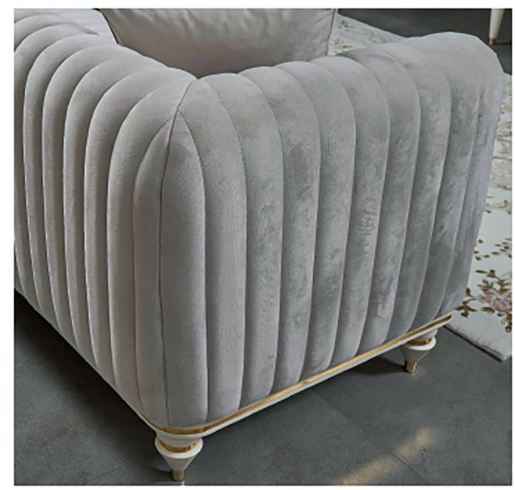 Gray tufted armchair with decorative legs on a dark floor.