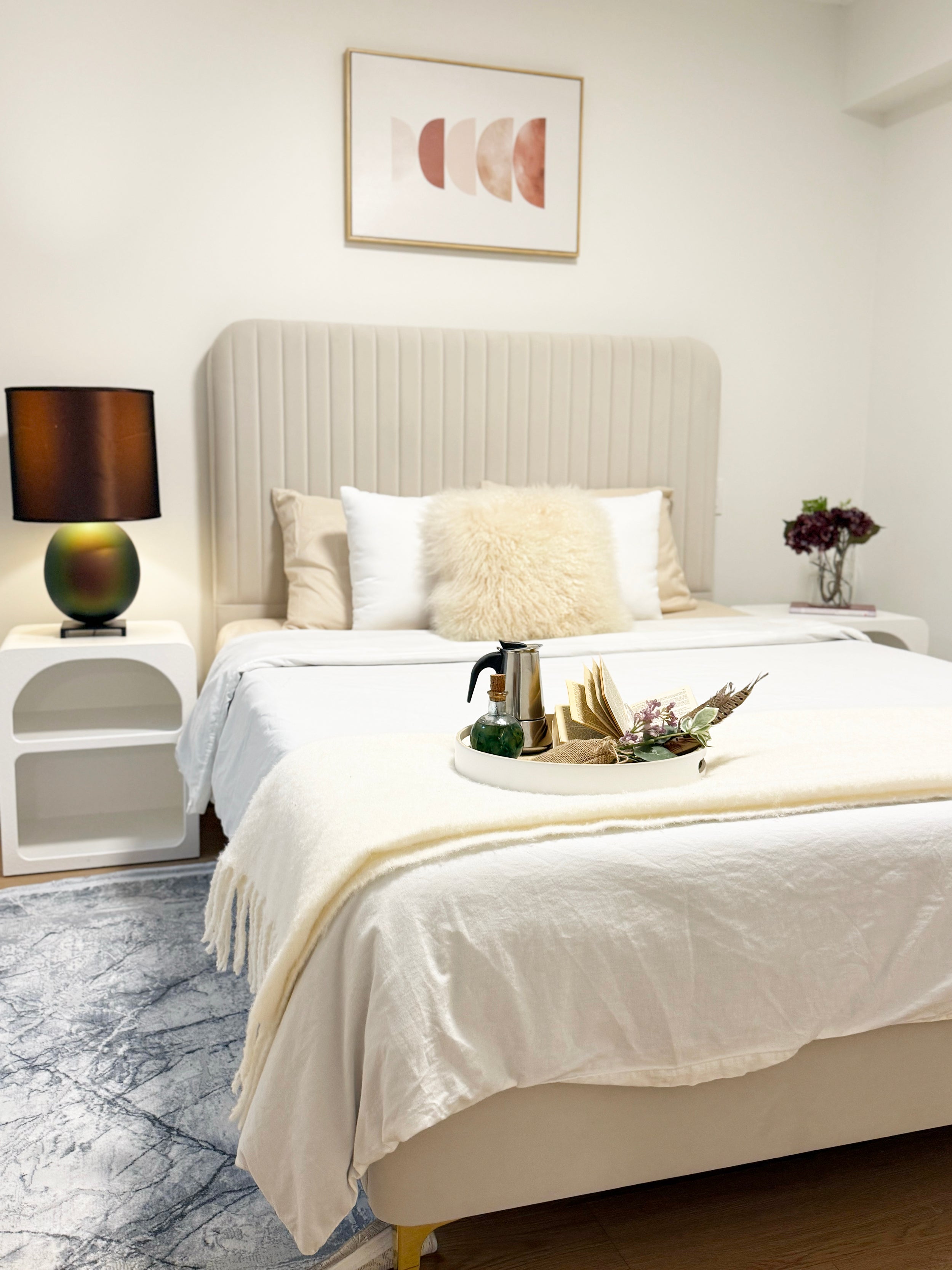 Neatly made bed in a bedroom with a lamp and decorative items on the nightstand.