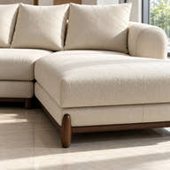 A close-up of a modern sectional sofa in a warm off-white textured fabric, showing the chaise lounge, back cushions, and dark wood legs on a light tiled floor.